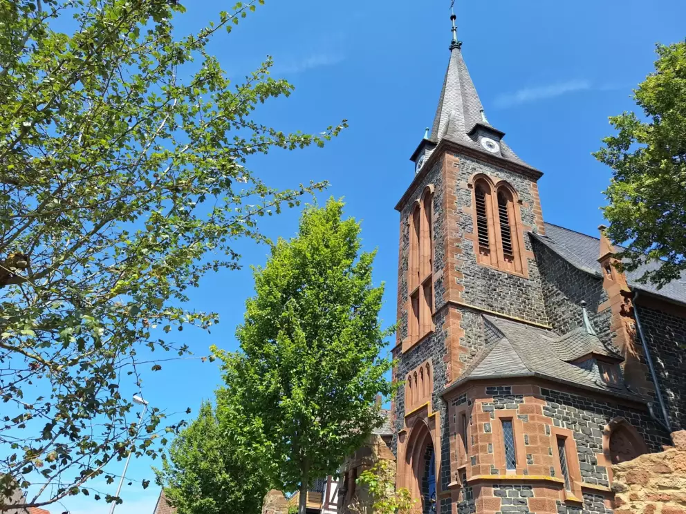 Spitzer Glockenturm der Kirche von Allendorf a.d. Landsburg mit 4 Fenstera.d. Landsburg mit 4 Fenstern, blauer Himmel und Bäumen im Vordergrund
