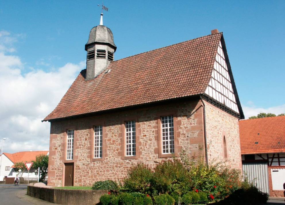Kleine Kirche aus Backstein, Rundbogenfenstern einem runden Kirchturm und Büschen im Vordergrund