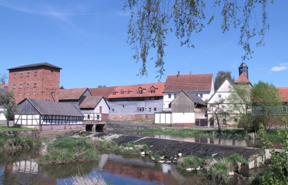 Wehr eines Flusses im Hintergrund eine Schlossanlage und ein alte Mühle aus Fachwerk